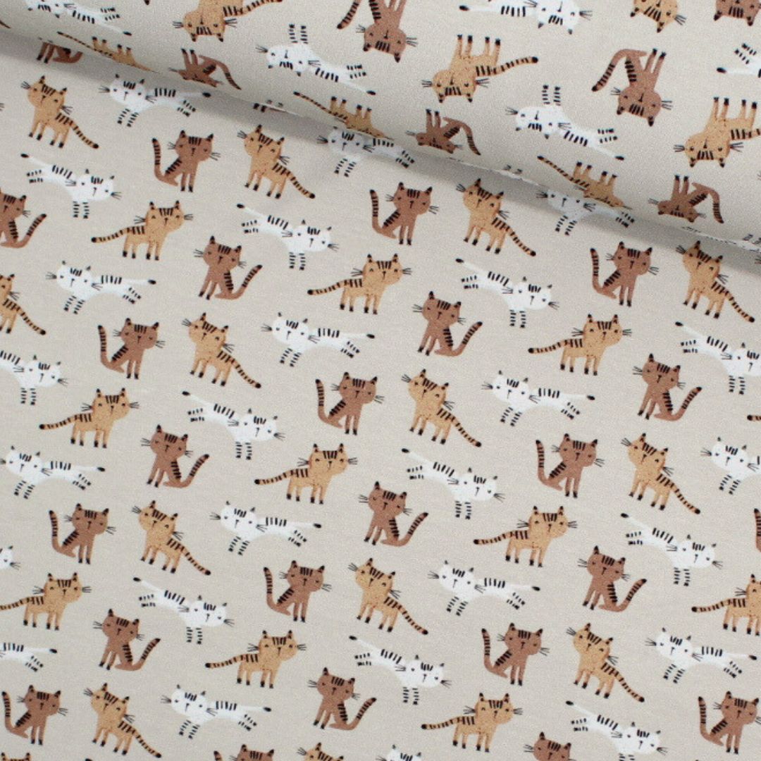 Der Jersey-Stoff mit niedlichen Katzen auf beigem Hintergrund, ideal für die Herstellung von Babykleidung und Leggings. Stoffball