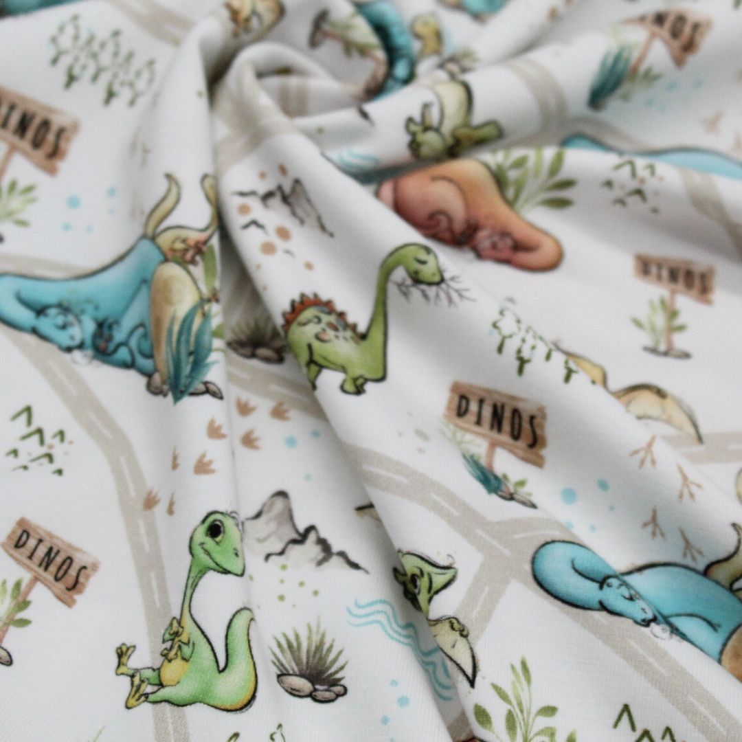Oeko-Tex zertifizierter Jersey-Stoff mit Dinosauriermotiven auf weußem Hintergrund, bequem und angenehm für Kinder.