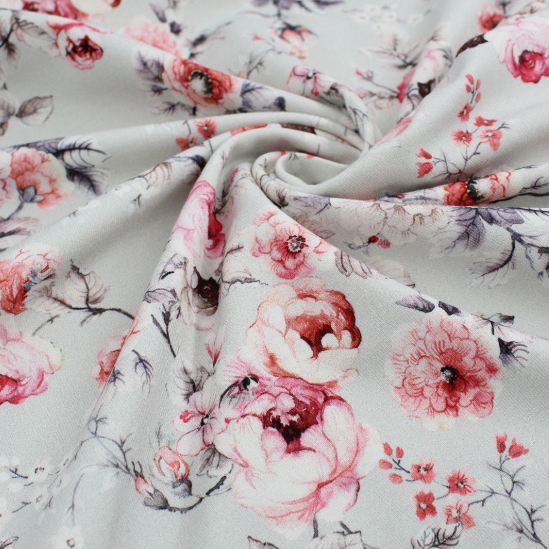 Detailaufnahme eines Baumwolljerseys mit pinken und roten Rosenmotiven auf grauem Stoff.