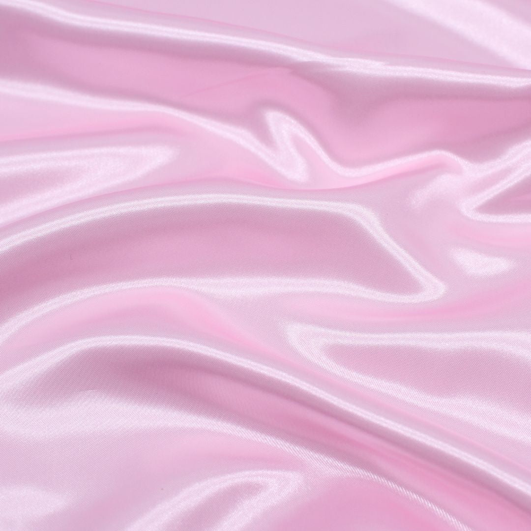 Nahaufnahme des glänzenden Satin-Stoffs in Hellrosa, ideal für Ballkleider und Dekorationen.