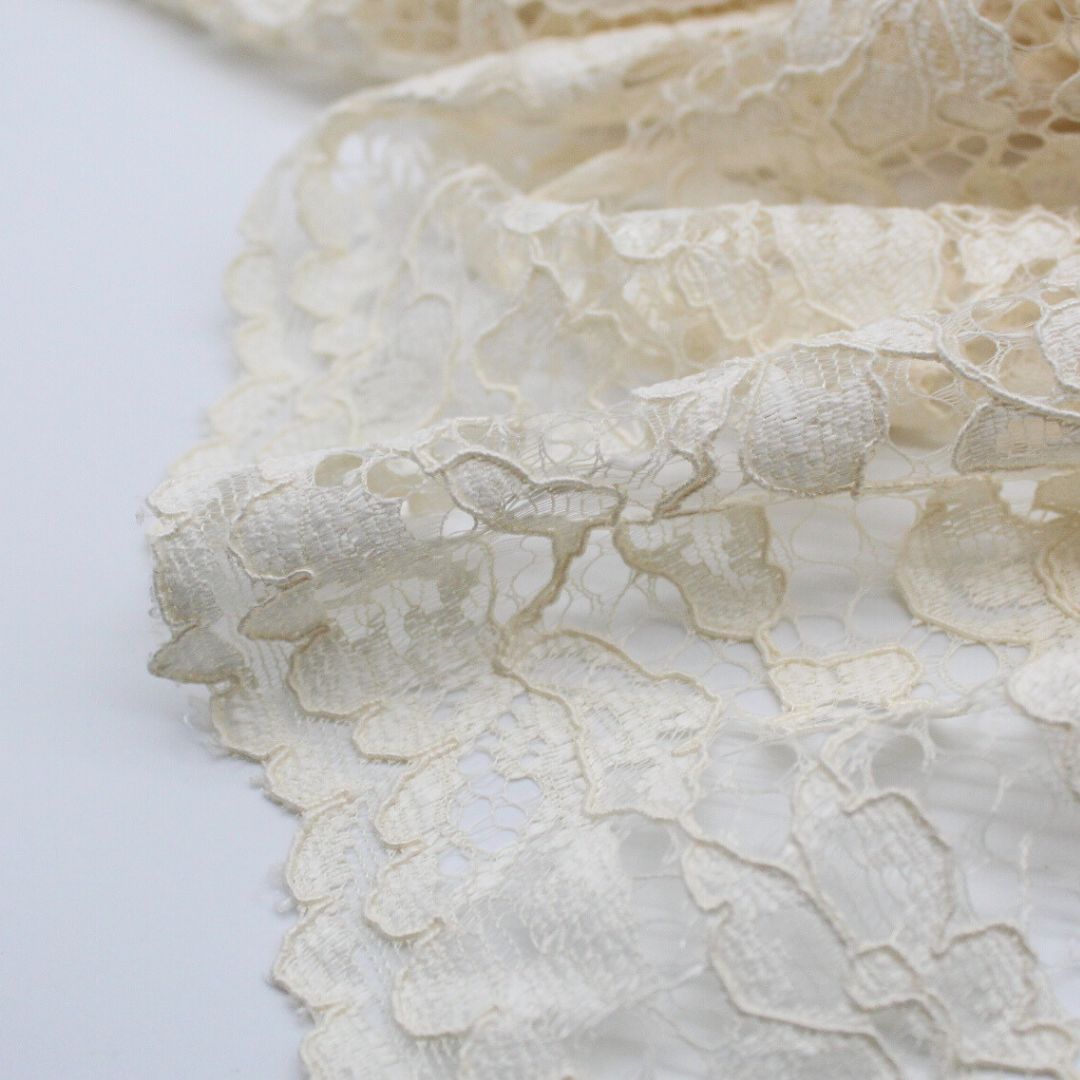 Nahaufnahme eines eleganten Spitzenstoffs mit filigranem Spitzensaum an beiden Seiten in zarter cremeweißer Farbe.