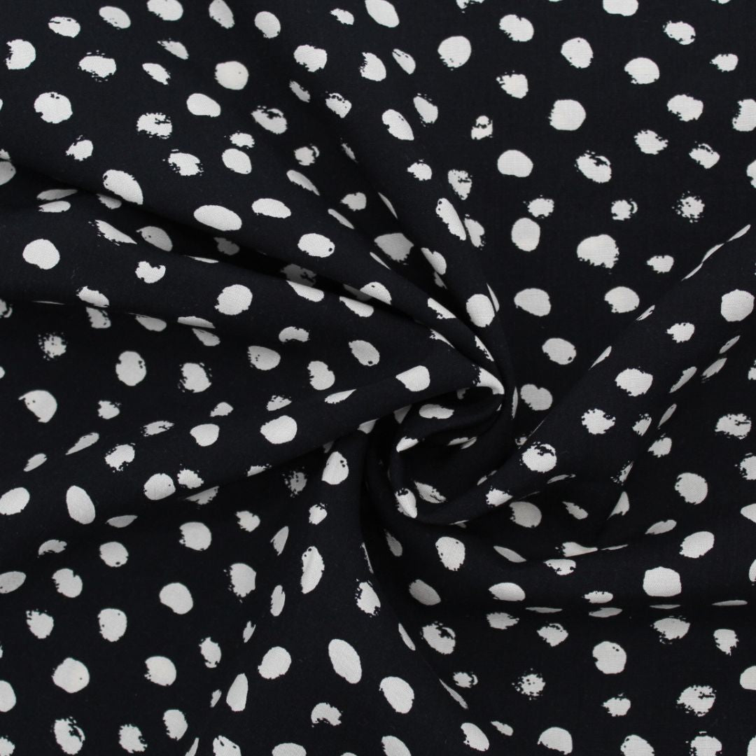 Viskosestoff mit kleinen unregelmäßigen Ecru-Punkten auf schwarzem Hintergrund, ideal für die Herstellung von Blusen, Kleidern und Röcken.