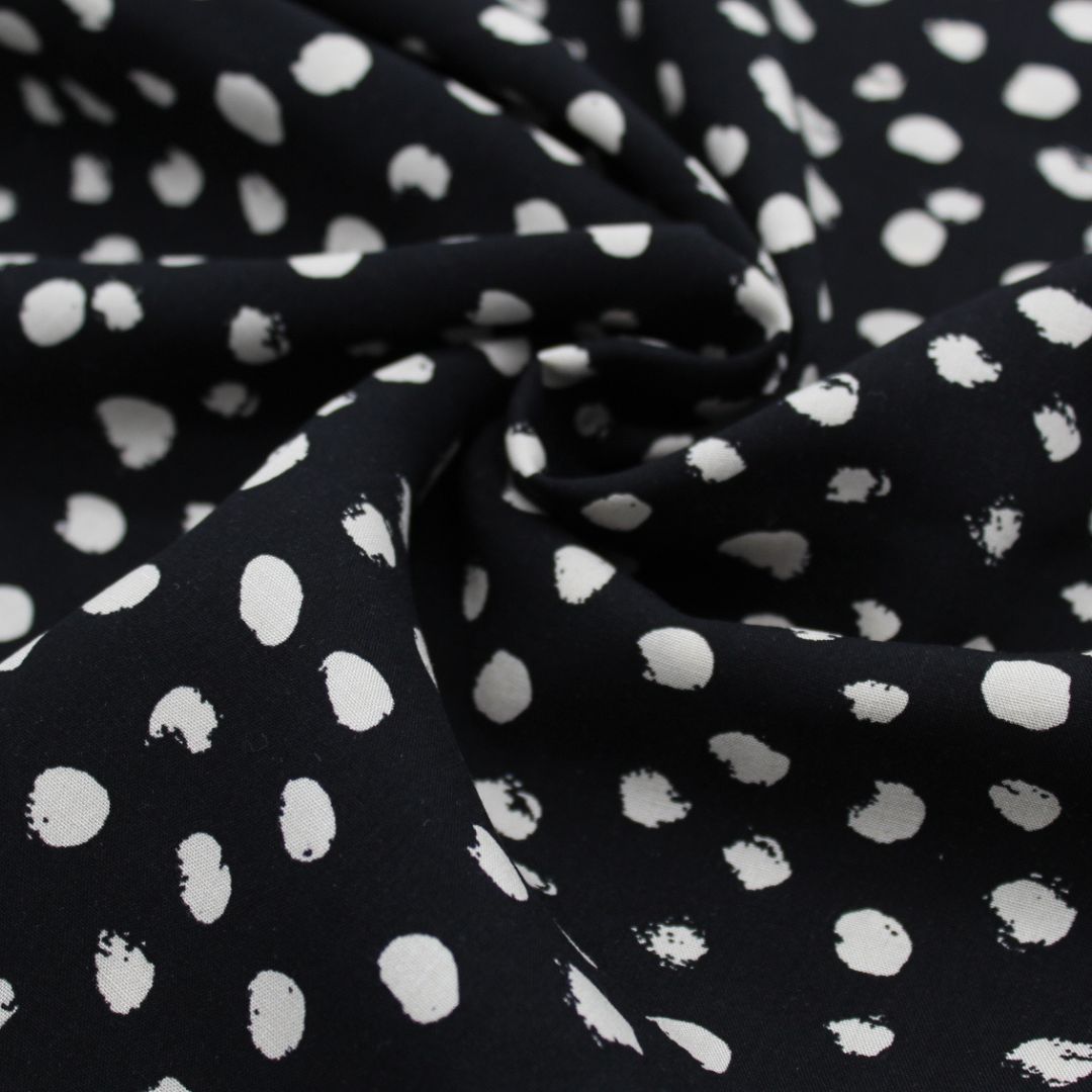 Viskosestoff mit kleinen unregelmäßigen Ecru-Punkten auf schwarzem Hintergrund, ideal für die Herstellung von Blusen, Kleidern und Röcken.