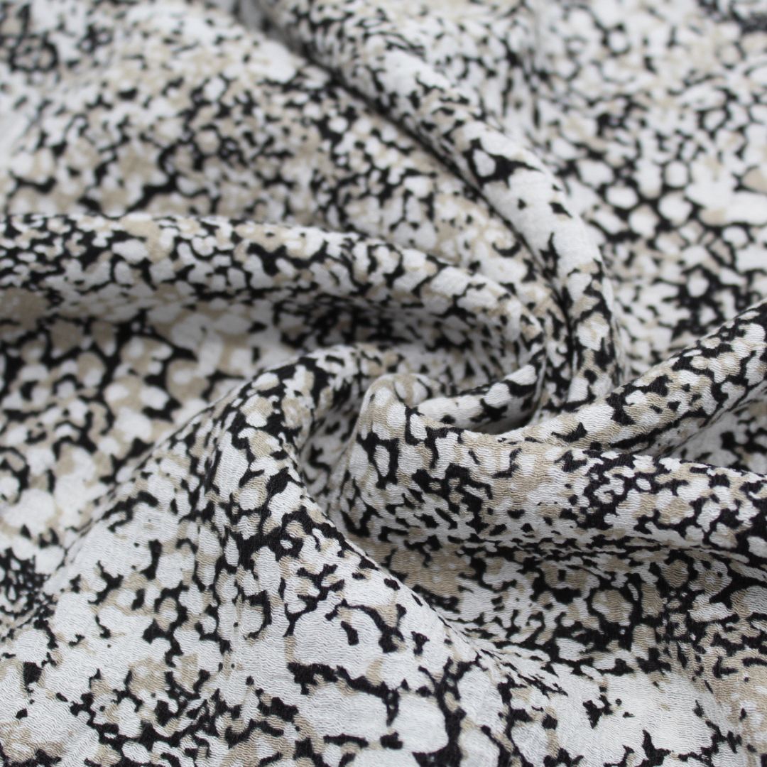Viskosestoff Crincle mit abstrakten Punkten in Sand, Schwarz und Cremeweiß, ideal für die Herstellung von Kleidern und Blusen.
