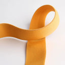 Vielseitiges Gummiband in 25 mm Breite in Senfgelb, weich und elastisch, ideal für Bekleidung und Bastelarbeiten.