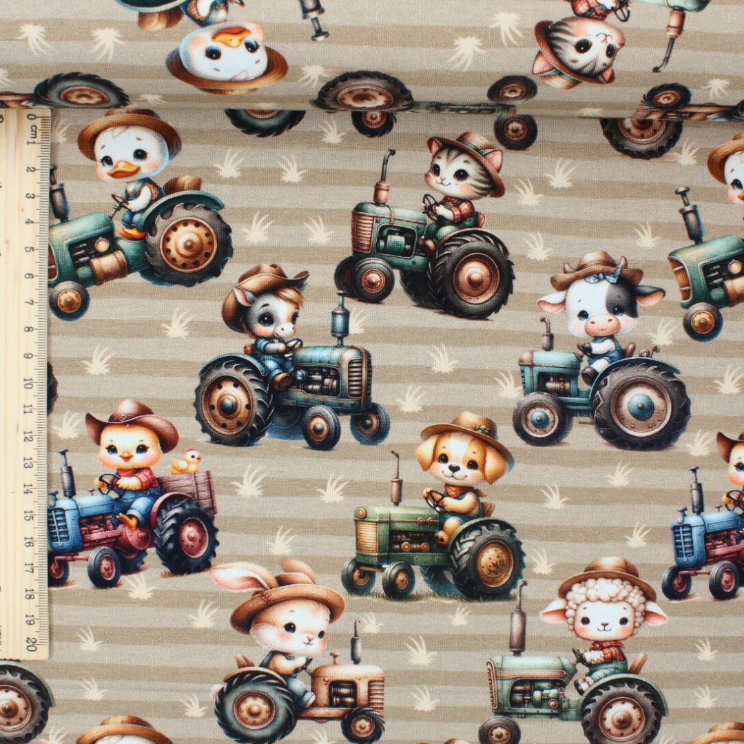 Detailansicht: Weicher Baumwolljersey mit Traktor- und Tiermotiven auf beigem Hintergrund. Lineal 