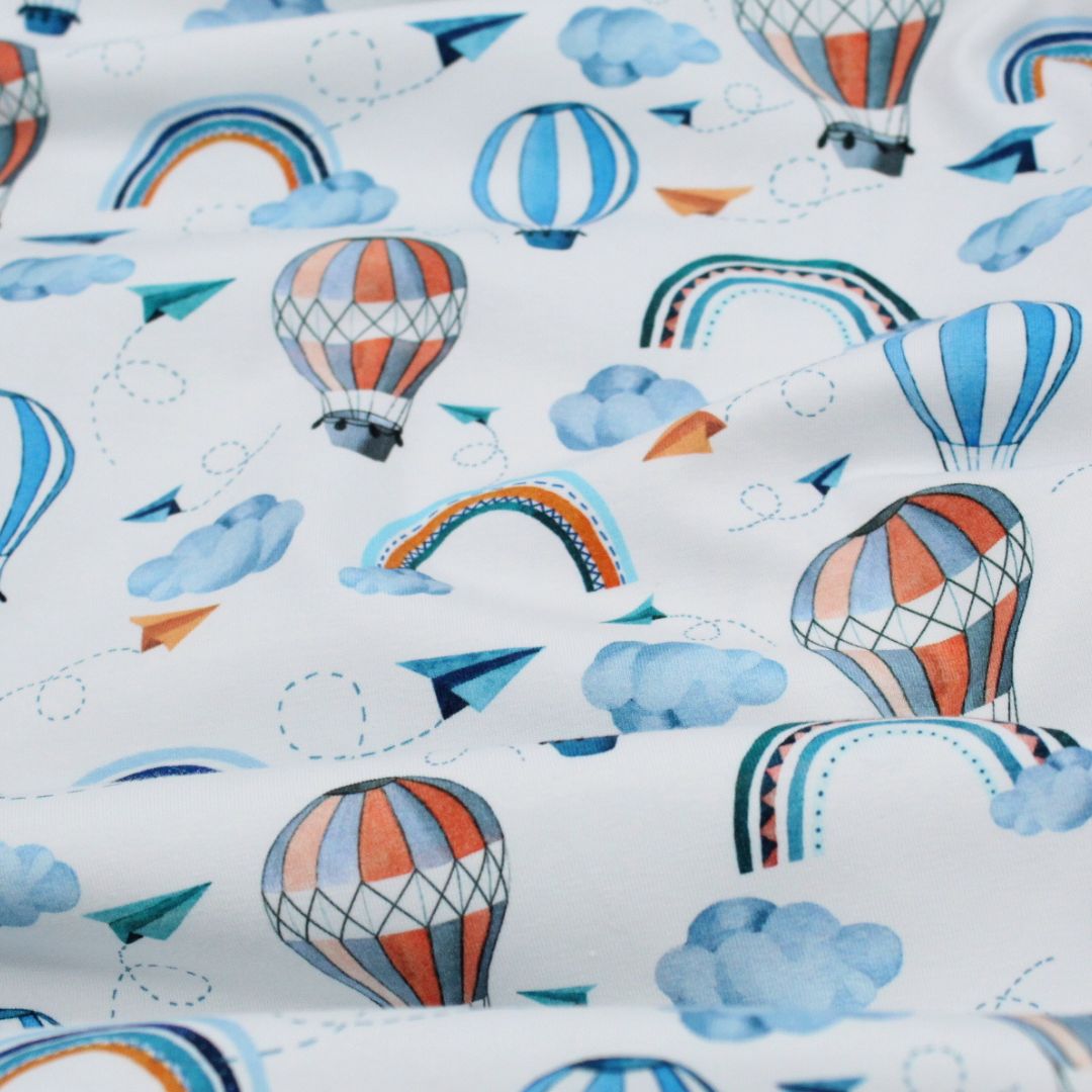 Jersey-Stoff mit Heißluftballons und Regenbögen in Blau auf weißem Hintergrund. Detailaufnahme des exklusiven Designs.