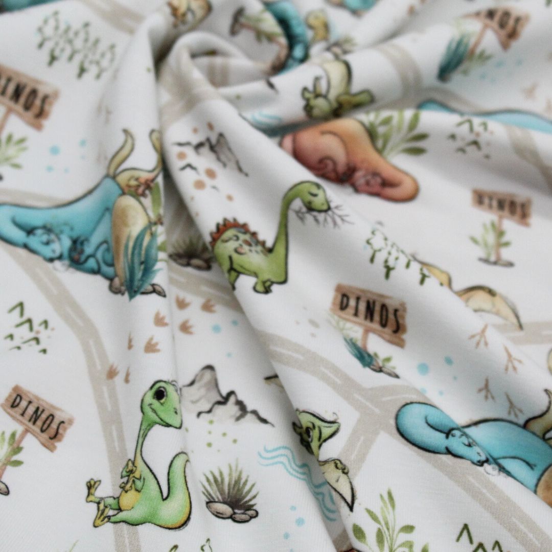 Oeko-Tex zertifizierter Jersey-Stoff mit Dinosauriermotiven auf weußem Hintergrund, bequem und angenehm für Kinder. 