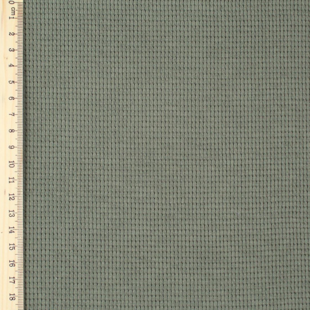 Gefalteter Mini Waffeljersey Stoff in Olivgrün, der die elastische und flexible Beschaffenheit zeigt. Lineal