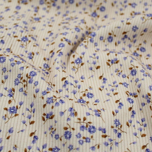 Weicher Rib Jersey Stoff mit kleinen blauen Blumen auf beige Hintergrund – ideal für feminine und romantische Kleidung.