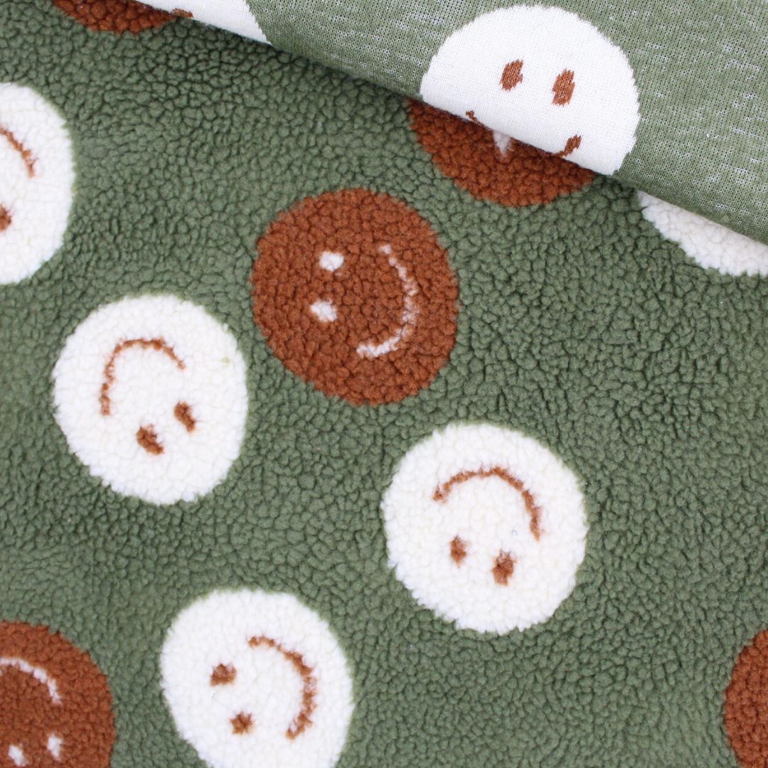 Teddy Bouclé Stoff „Happy Faces“ auf grünem Hintergrund – Smiley-Muster, weicher Kuschelstoff Meterware
