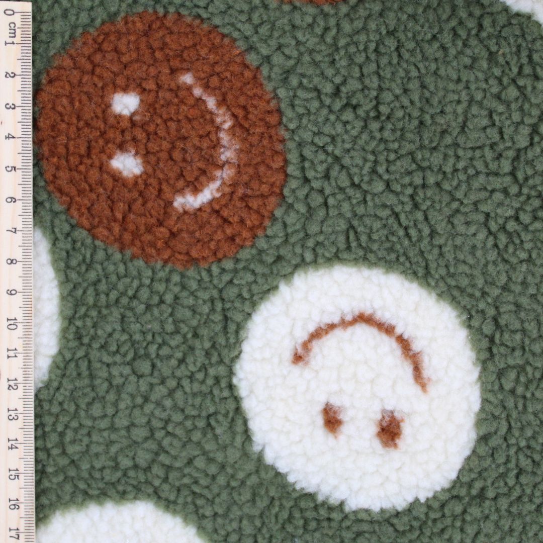 Nahaufnahme der Teddy Bouclé Struktur mit Happy-Faces-Motiv – flauschiger Stoff in Grün