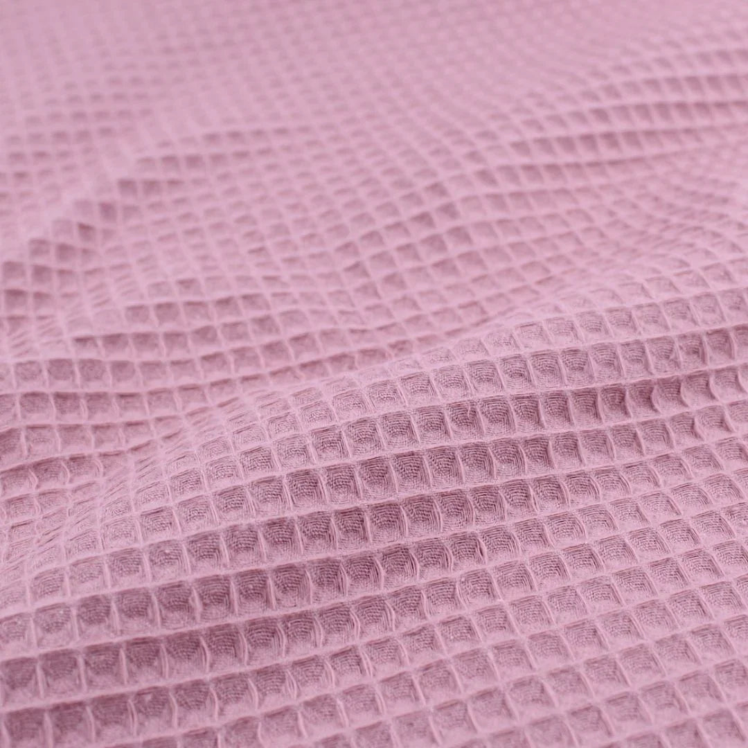 Detailansicht eines hochwertigen Waffelpique-Stoffs in Rosa mit dreidimensionaler Wabenstruktur.
