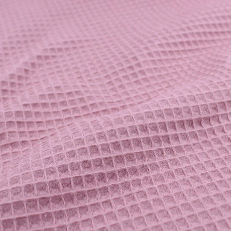 Detailansicht eines hochwertigen Waffelpique-Stoffs in Rosa mit dreidimensionaler Wabenstruktur.