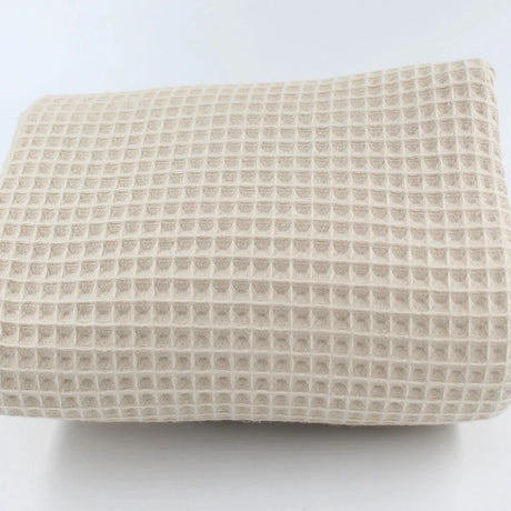 Detailansicht eines hochwertigen Waffelpique-Stoffs in Hellbeige mit dreidimensionaler Wabenstruktur.